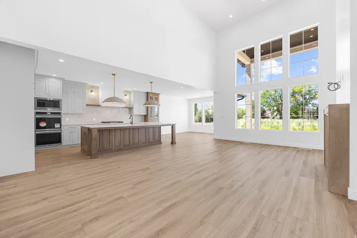 Vaulted ceilings, extensive window array, wood-finish flooring, built-in kitchen appliances, and a substantial kitchen island with integrated sink