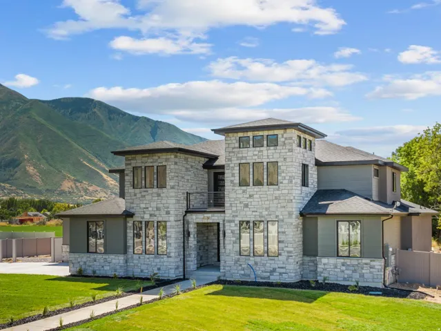 Stone and stucco exterior with multiple large windows, a prominent central tower, and a spacious green lawn