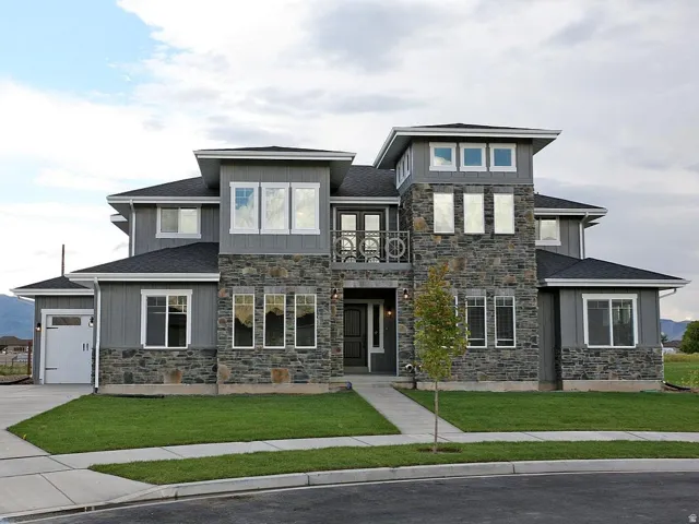 Contemporary exterior featuring stone and siding finishes, multiple windows, a prominent front entry with a balcony, and an attached garage with a paved driveway