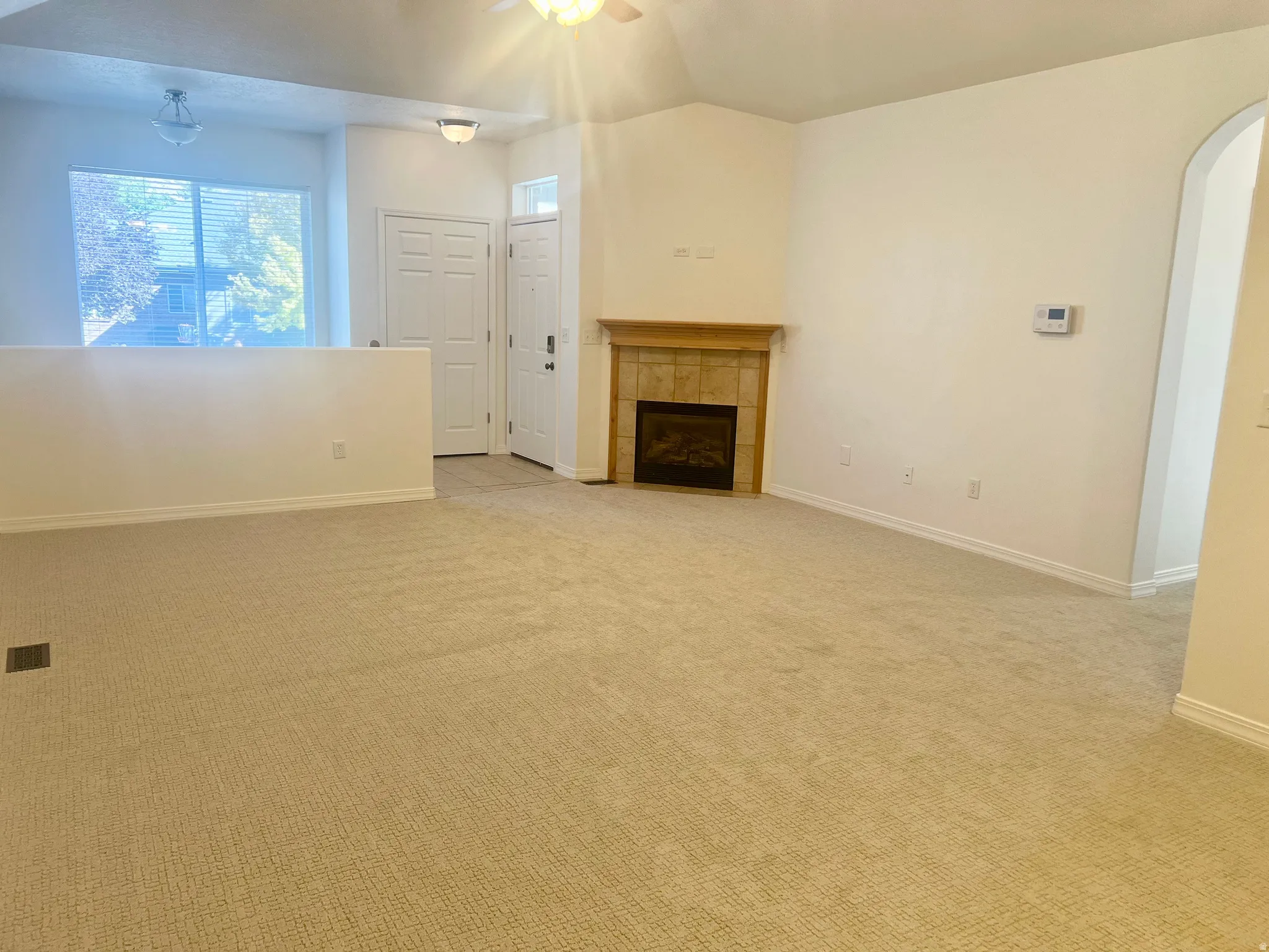 Carpeted living area featuring a built-in fireplace with a tile surround and wood mantel, vaulted ceiling, and an arched entry