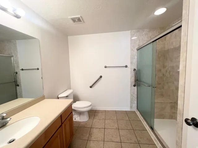 Walk-in shower with glass enclosure, single vanity with integrated sink, and tile flooring