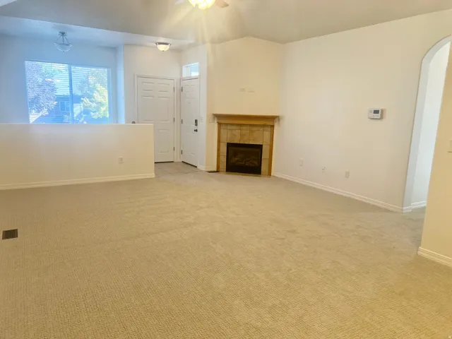 Carpeted living area featuring a built-in fireplace with a tile surround and wood mantel, vaulted ceiling, and an arched entry