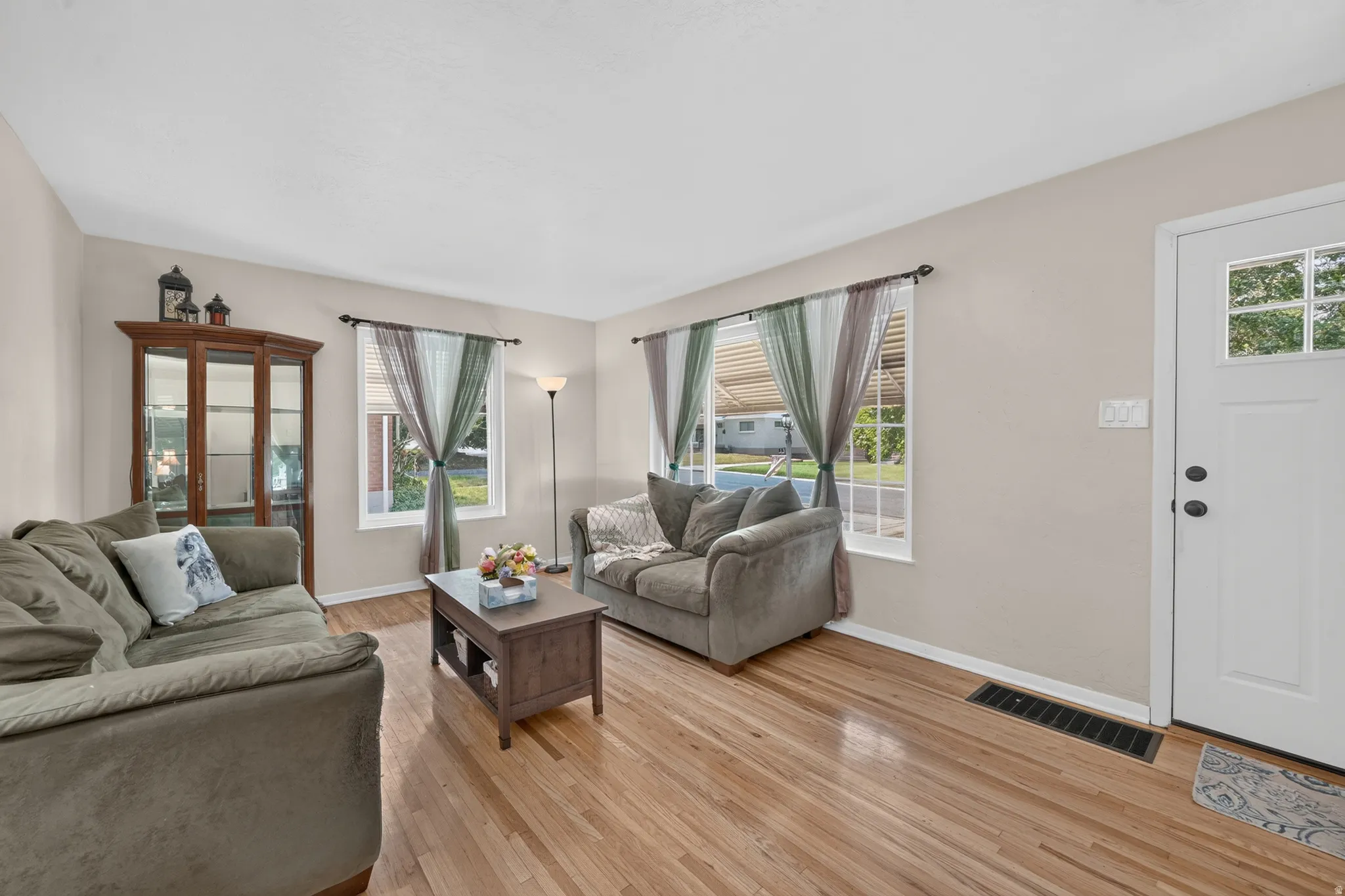 Hardwood flooring throughout, multiple windows providing natural light, a white entry door with upper window panes, and light-toned wall paint