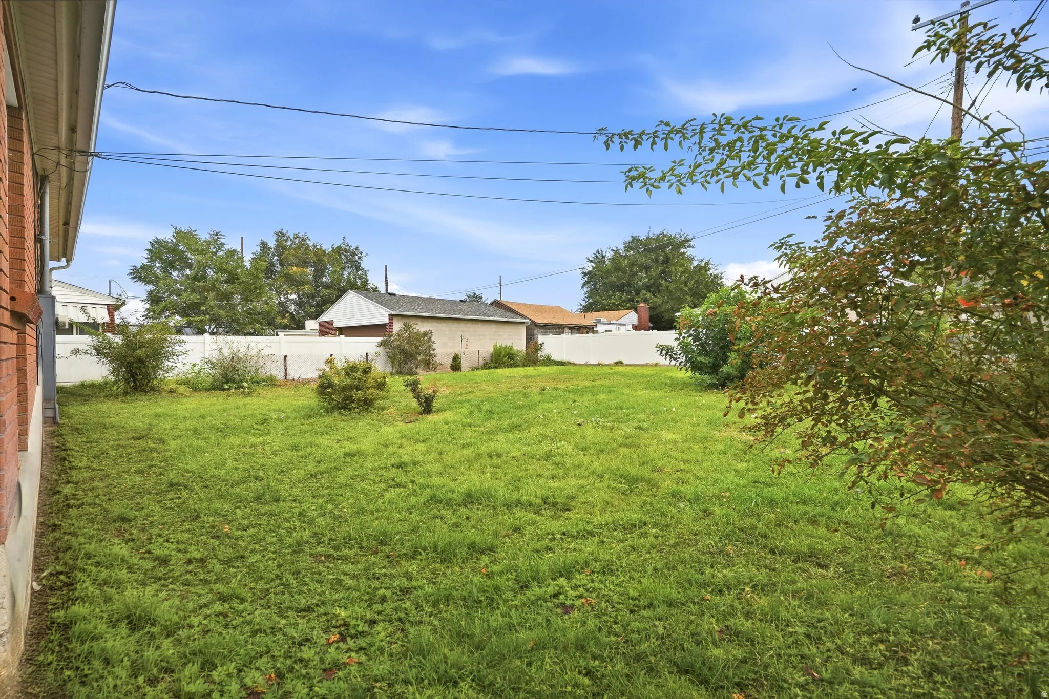 Expansive lawn with perimeter fencing, mature trees, and a detached structure