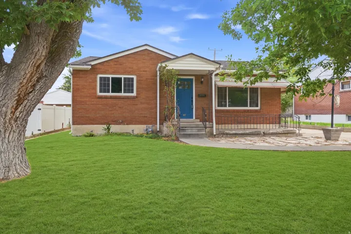 Brick exterior, blue front door, stone patio, wrought iron railings, and a manicured lawn