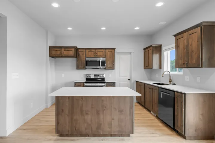 Kitchen featuring wood-finish cabinetry, stainless steel appliances, a center island with a solid surface countertop, and recessed lighting