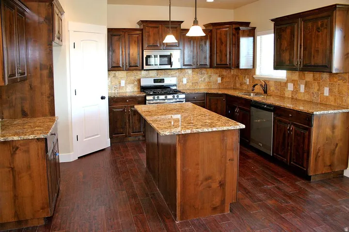Kitchen featuring wood-finish cabinetry, granite countertops, a tiled backsplash, stainless steel appliances, and a central island