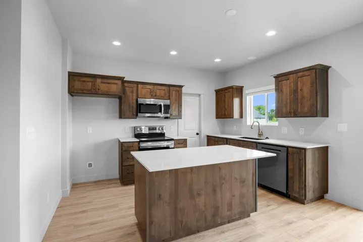 Kitchen featuring wood-finish cabinetry, stainless steel appliances, recessed lighting, and a center island with a light-toned countertop