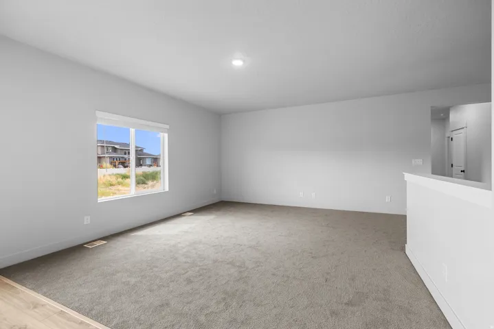 Spacious room with light gray carpeting, recessed ceiling lighting, a large window, and a partial wall with a cap