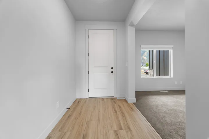 Two-panel interior door, wood-finish flooring, neutral wall tones, recessed window with blinds, and carpeting