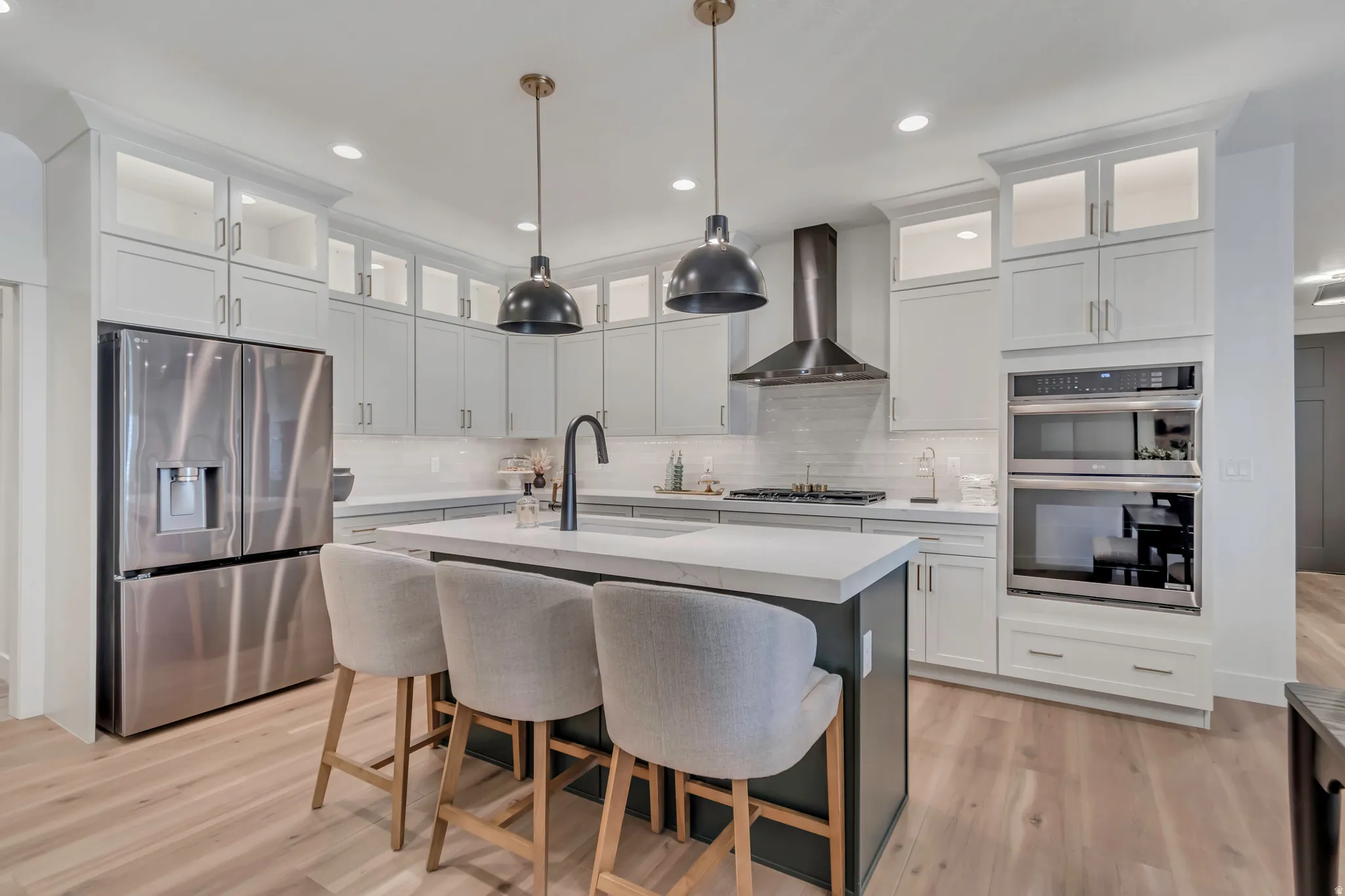 Gourmet kitchen with stainless steel appliances, light wood-finish flooring, white cabinetry with glass-front uppers, and a kitchen island with seating
