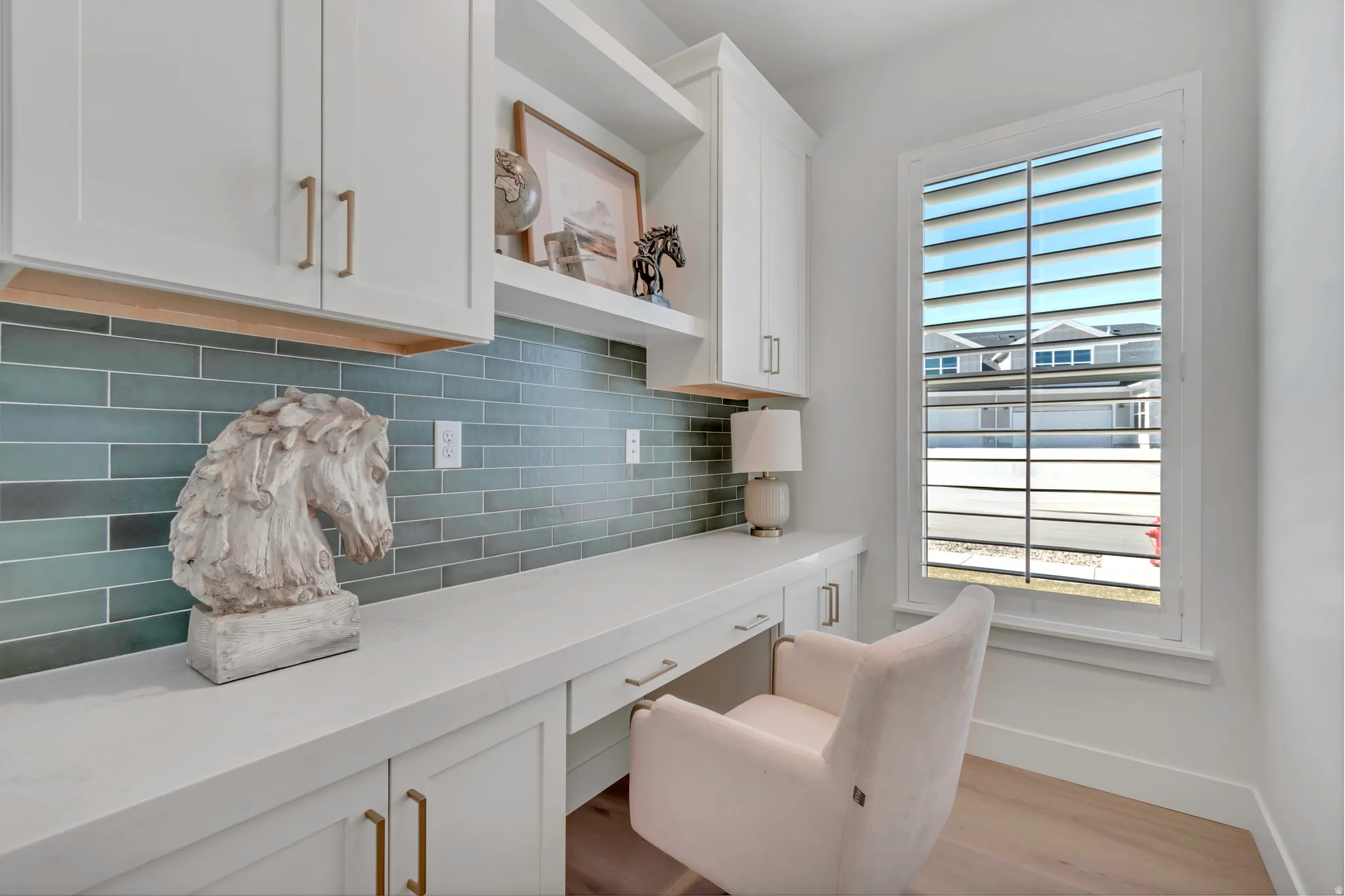 Built-in white cabinetry with gold-finish hardware, solid surface countertop, blue subway tile backsplash, and light wood-finish flooring