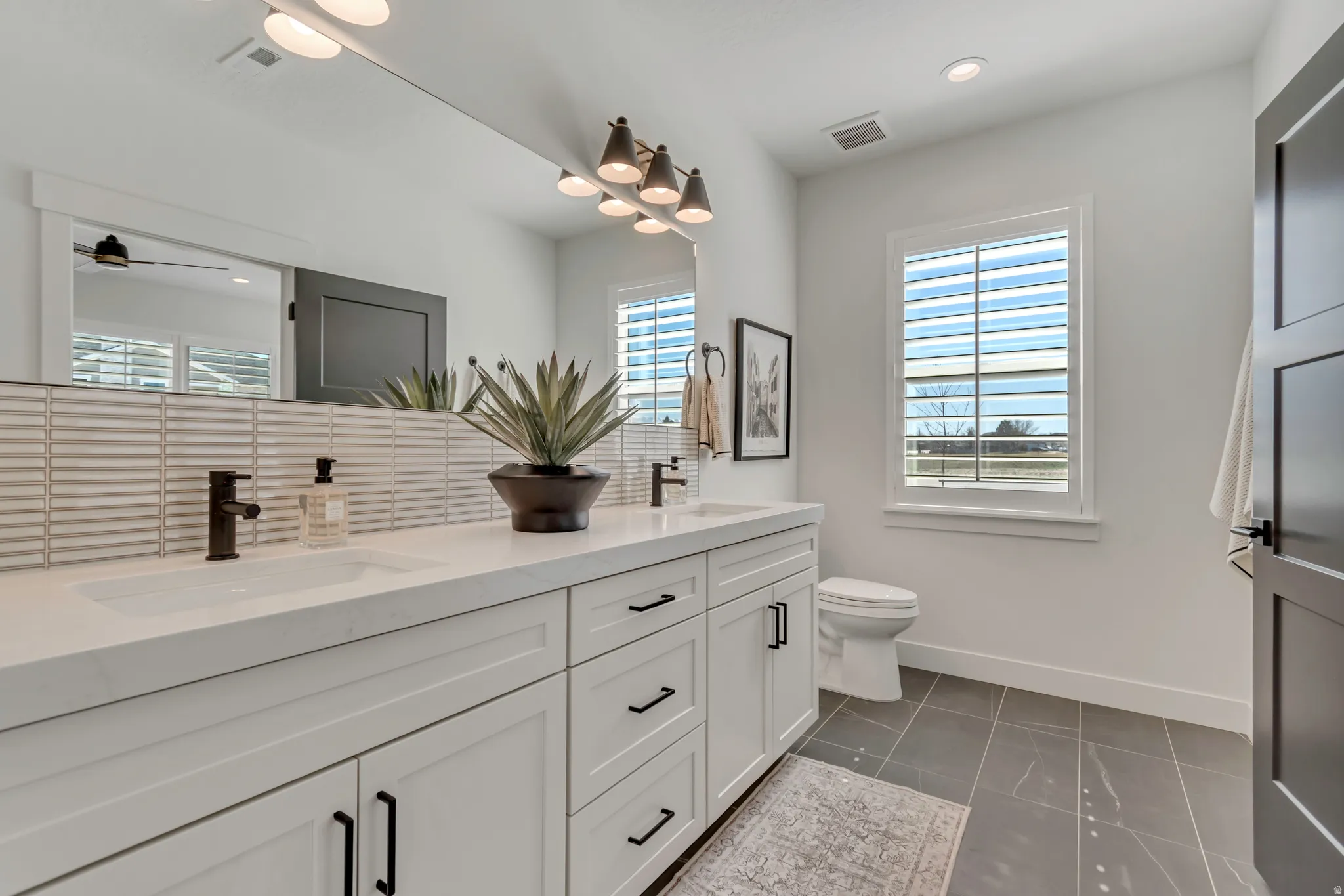 Dual vanity with white cabinetry and black hardware, white countertops, tile backsplash, and dark bronze fixtures