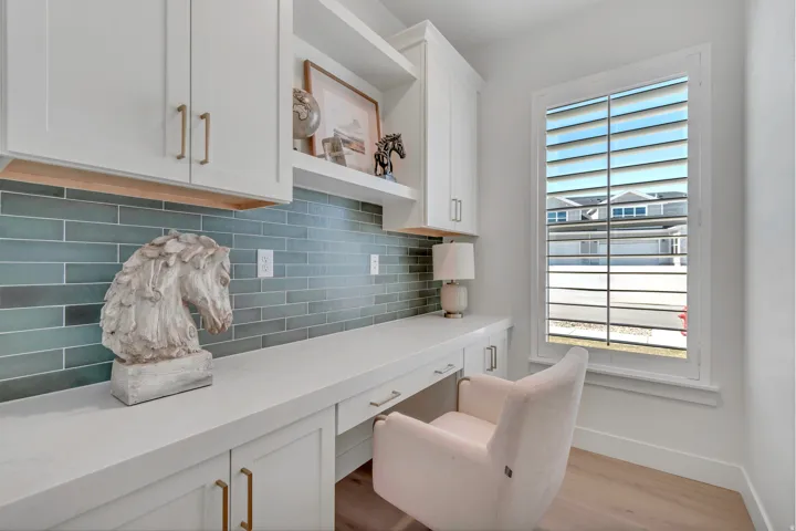 Built-in white cabinetry with gold-finish hardware, solid surface countertop, blue subway tile backsplash, and light wood-finish flooring