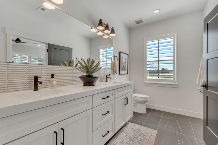 Dual vanity with white cabinetry and black hardware, white countertops, tile backsplash, and dark bronze fixtures