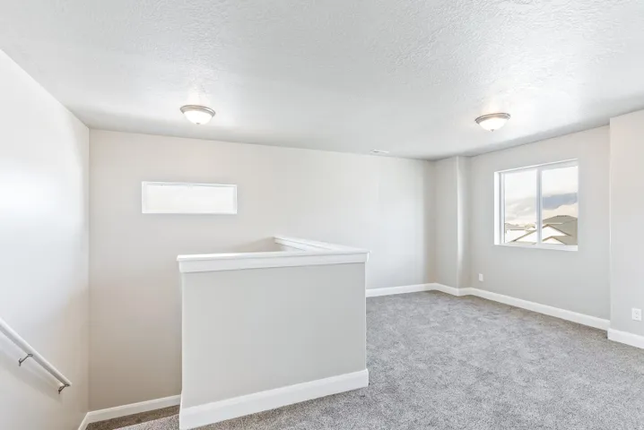 Carpeted landing area featuring a white window frame, wall-mounted light fixtures, and a white handrail
