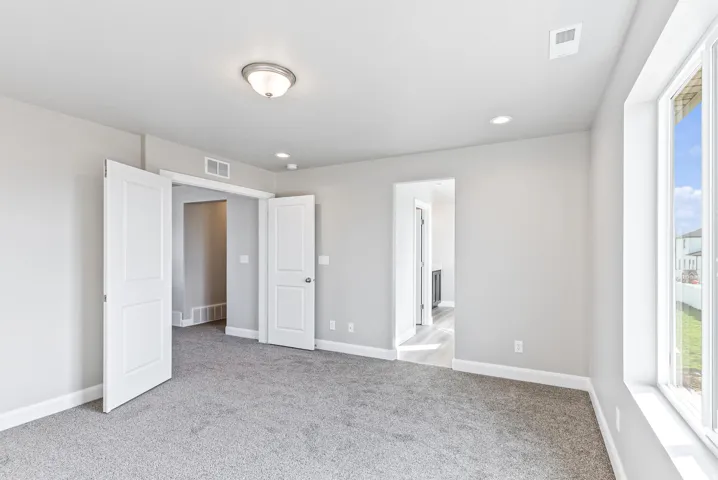 Recessed lighting, flush-mount ceiling fixture, grey carpeting, white trim, and a window providing natural illumination