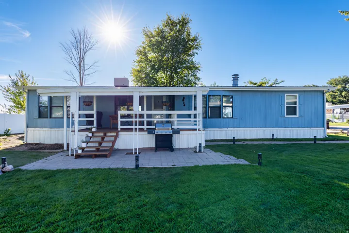Expansive lawn area with a paver patio and a covered porch featuring white railings and wood stairs