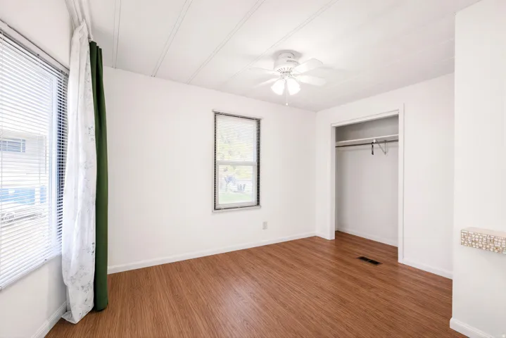 Wood-finish flooring, white walls, and a ceiling fan with integrated lighting