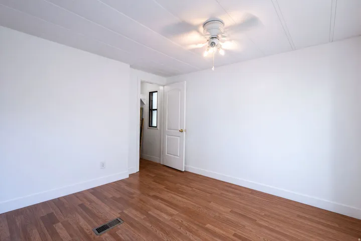 Wood-finish flooring, white painted walls, ceiling fan with integrated lighting, and a paneled door