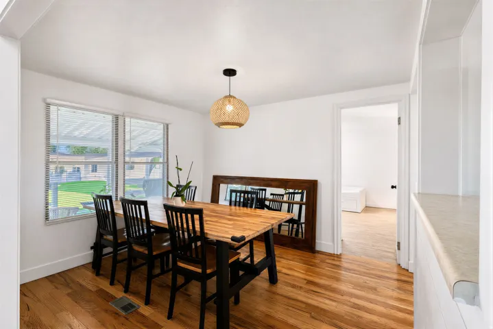 Hardwood flooring, dual windows with blinds, a woven pendant light fixture, white walls, and built-in shelving