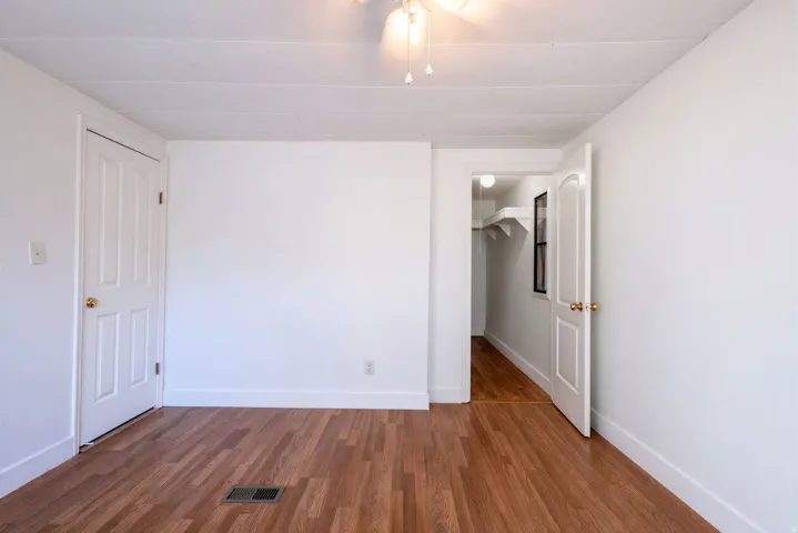 Wood-finish flooring, white paneled doors, ceiling fan with light fixture, and a built-in closet with shelving