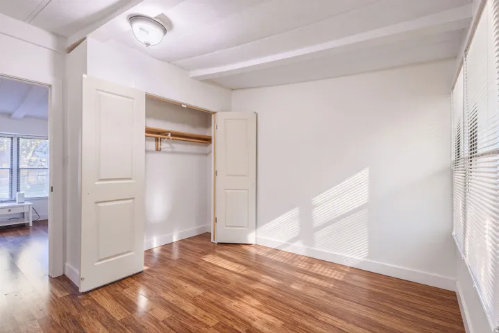 Wood-finish flooring with white baseboards, visible wood beams, and a window with blinds