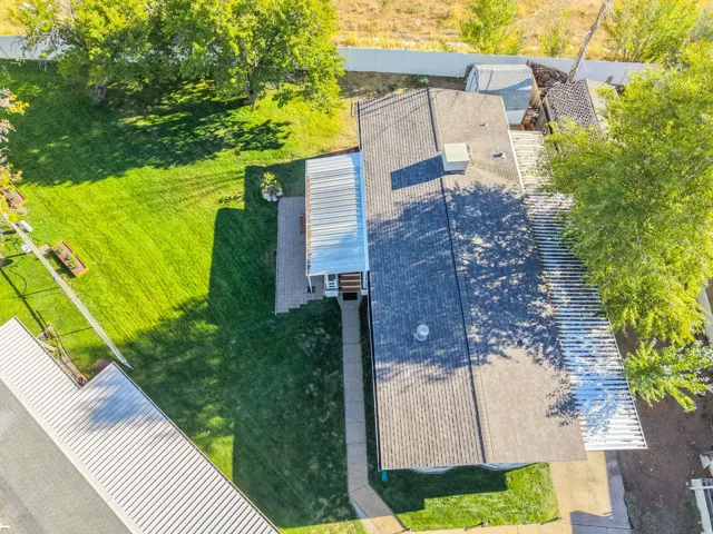 Gabled shingle roof with an extended metal awning, concrete path, and a grass lawn with mature trees