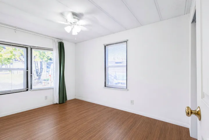 Wood-finish flooring, white walls, and a ceiling fan with integrated lighting