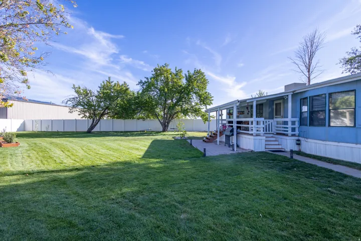 Expansive lawn area, mature trees, white privacy fencing, covered patio, and stepped access