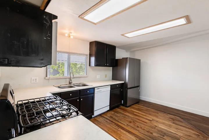 Stainless steel refrigerator, built-in dishwasher, gas range, dual basin sink, and wood-finish flooring