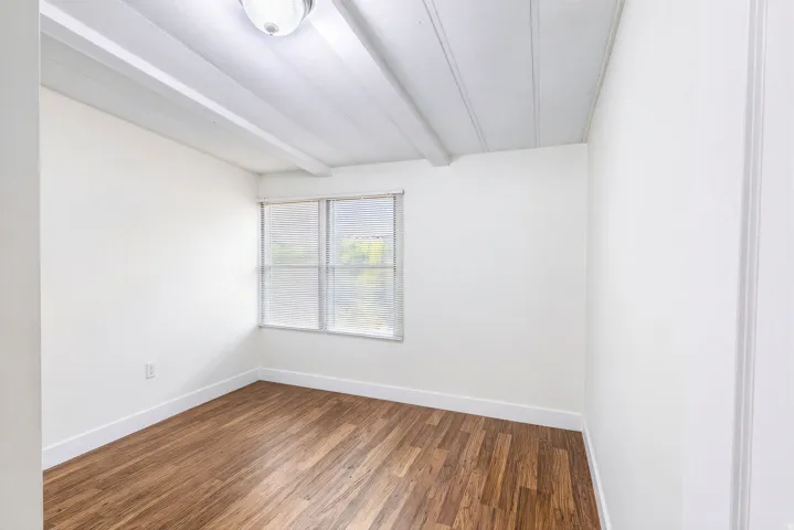 Wood-finish flooring, white walls, and a window with blinds
