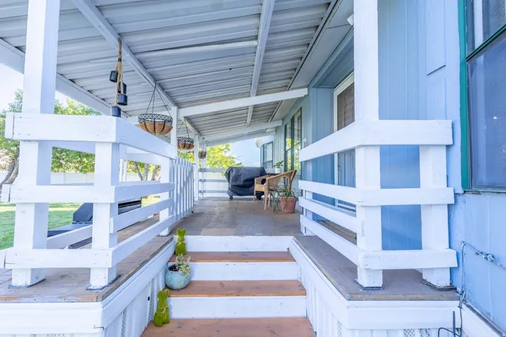 Covered porch with white railings, wood-finish steps, and light blue siding