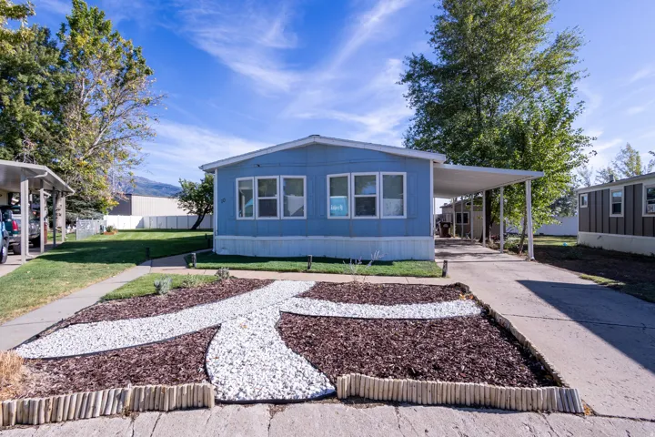 Light blue exterior, multiple windows, covered carport, concrete driveway, and landscaped front yard with wood chip and white stone accents