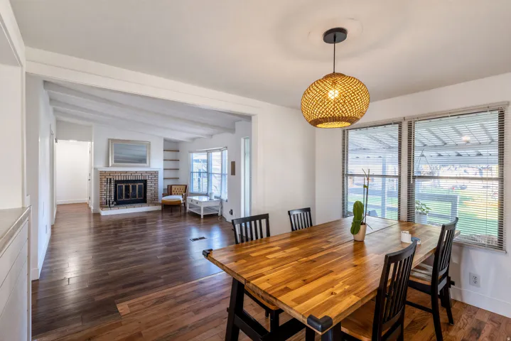 Wood-finish flooring throughout, living area with exposed beam ceiling, brick fireplace, built-in shelving, and multiple windows
