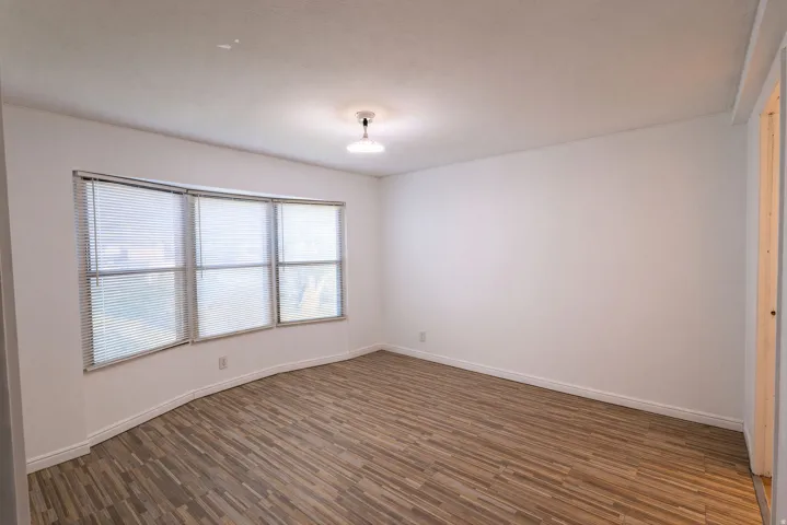 Bay window with horizontal blinds, wood-finish flooring, and a flush-mount ceiling light