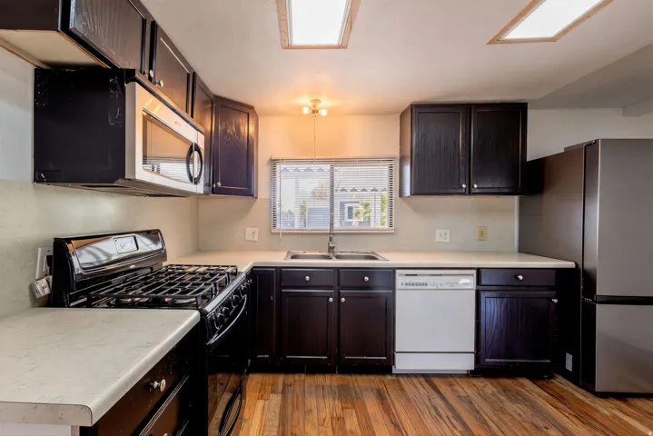 Kitchen featuring wood-finish flooring, dark cabinetry, light countertops, and a stainless steel refrigerator