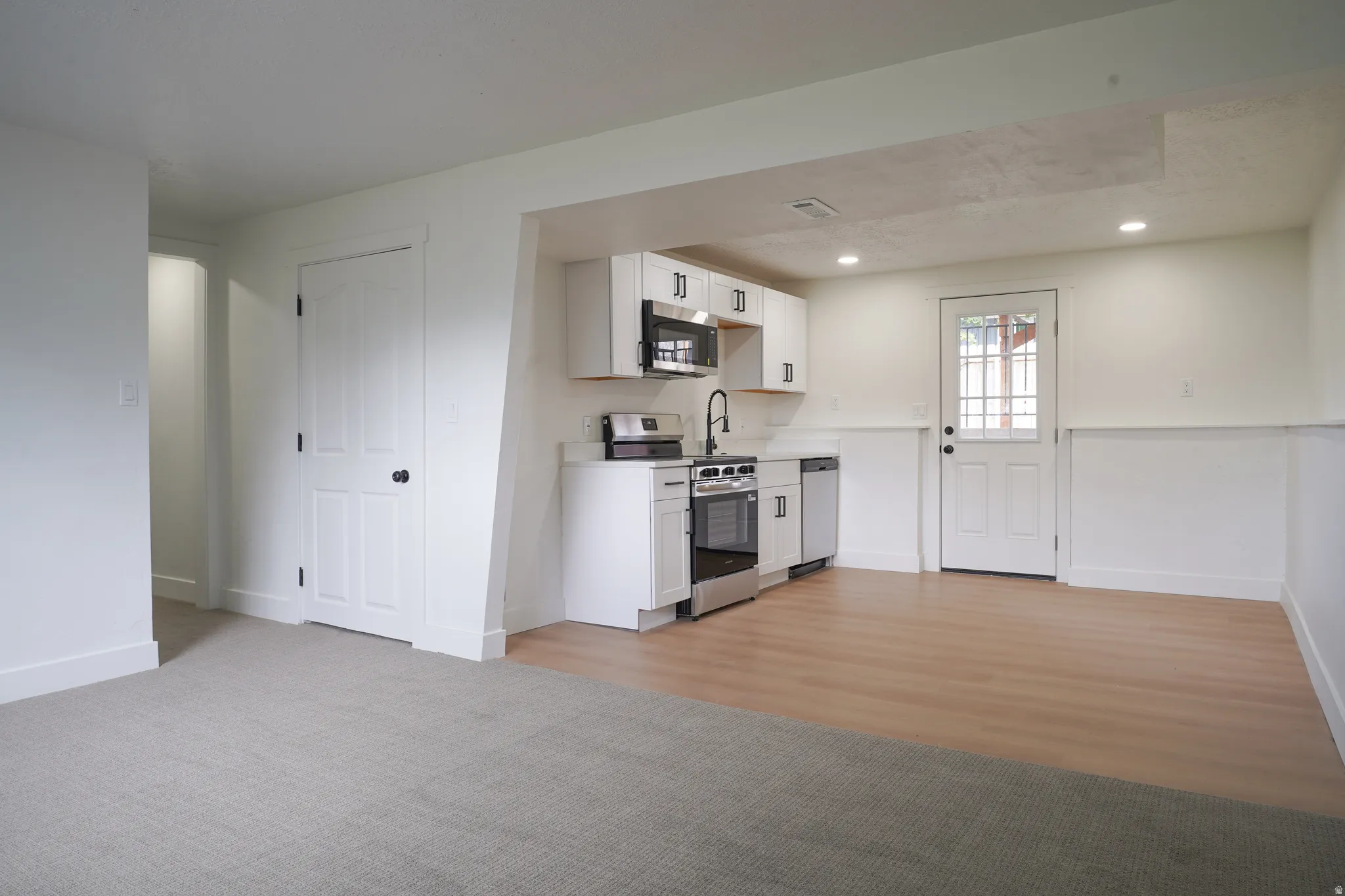 Galley kitchen with stainless steel appliances, white cabinetry, and wood-finish flooring