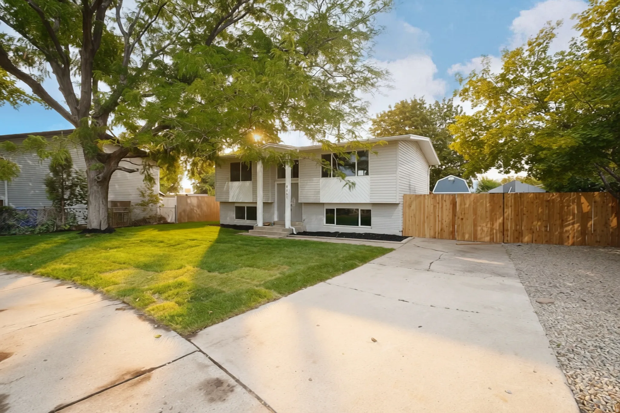 Split-level residence featuring white siding, a concrete driveway, and a wood privacy fence