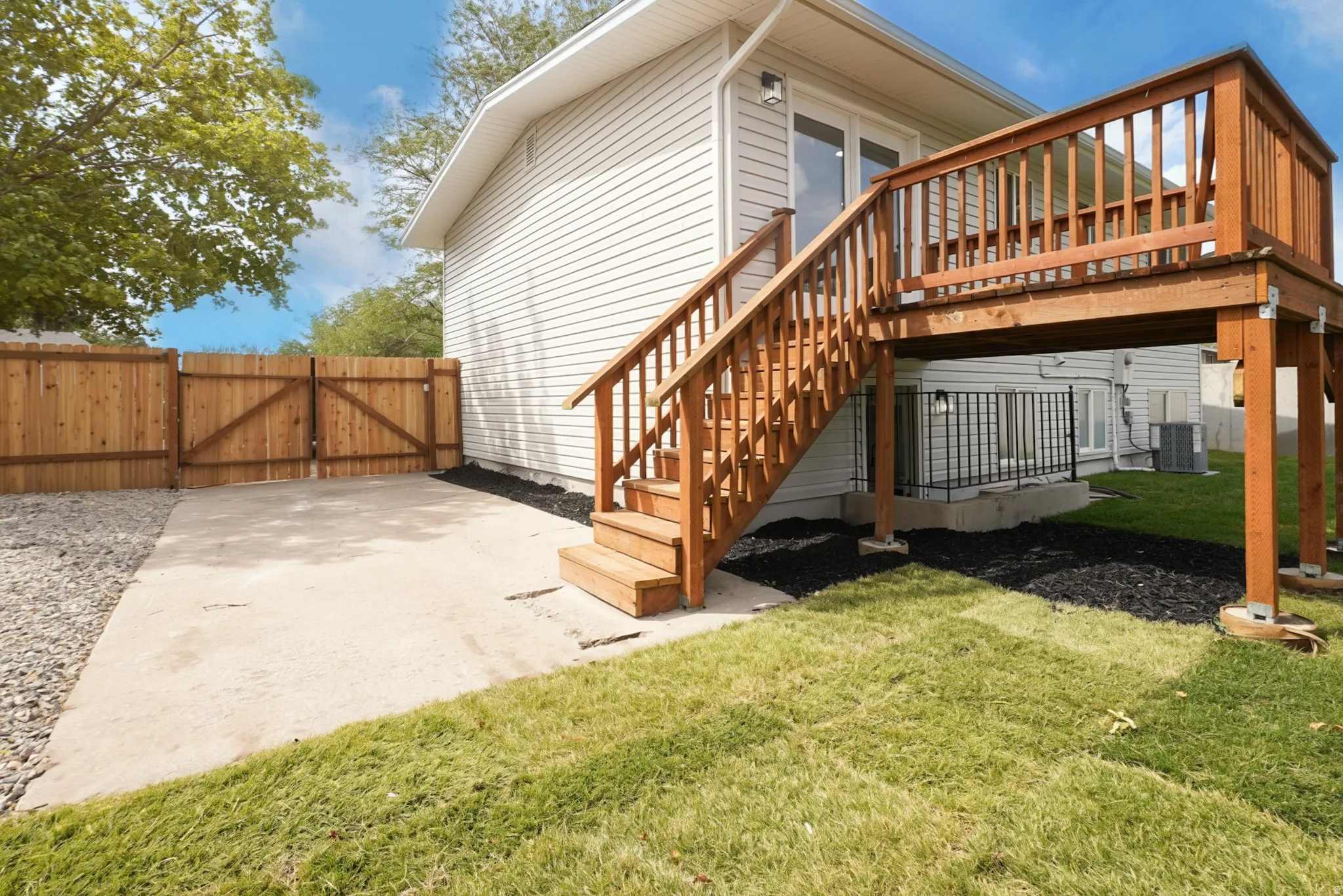 Rear exterior featuring vinyl siding, an elevated wood deck with stairs, a concrete patio, and a wood privacy fence with double gates