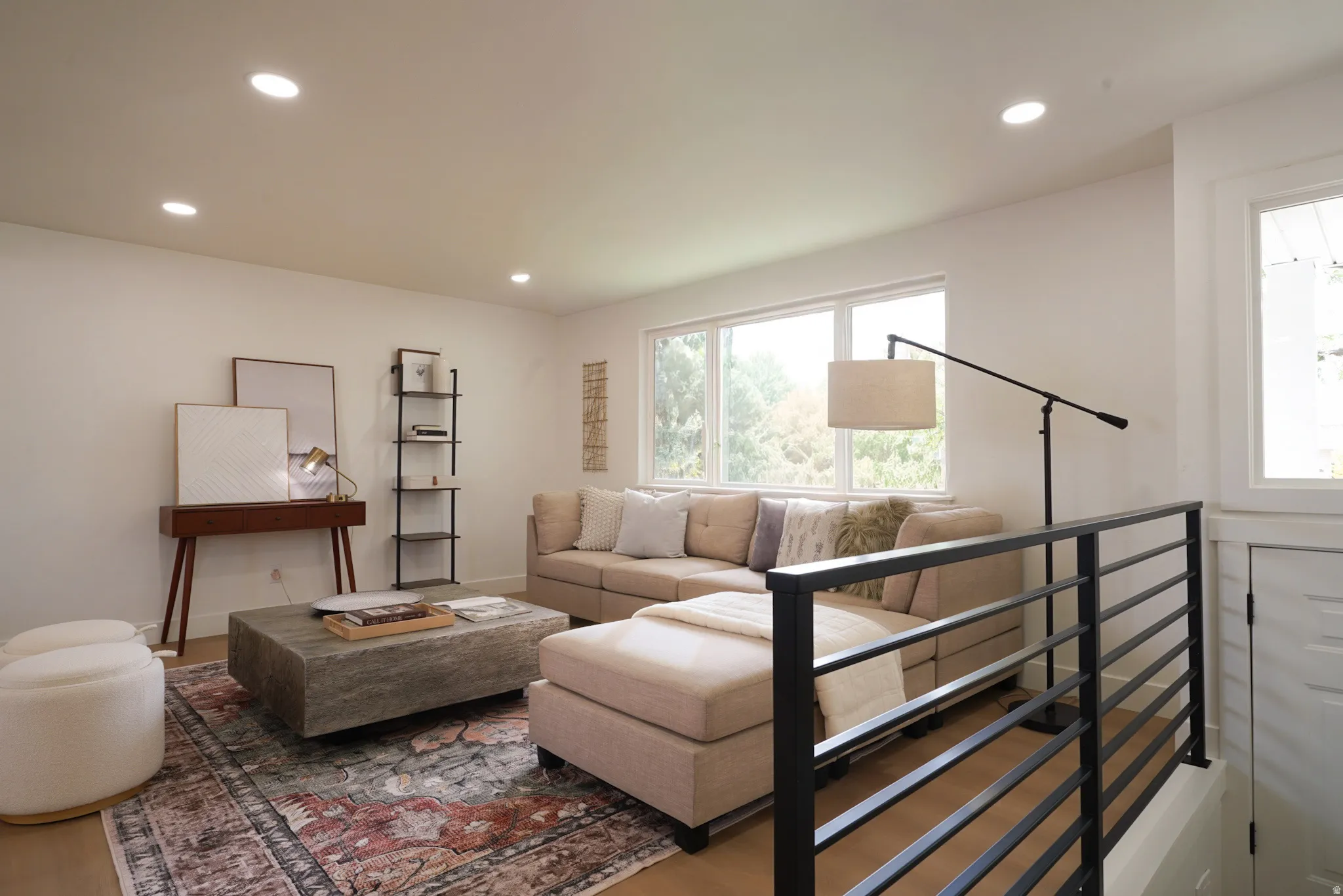Recessed lighting illuminates this bright living space featuring light wood-finish flooring and multiple windows