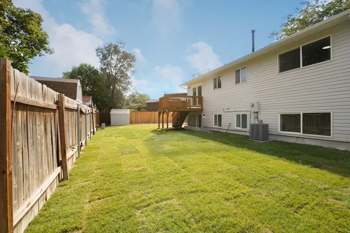 Expansive grassy yard with wood fencing, vinyl siding exterior, multiple windows, and a raised wood deck
