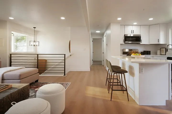 Recessed lighting, wood-finish flooring, white cabinetry, stainless steel microwave, and a kitchen island with a light-toned countertop