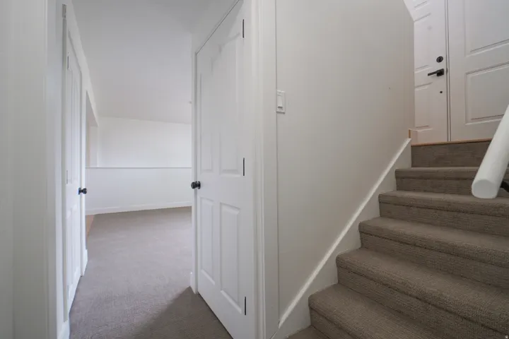 Carpeted staircase, white interior doors with black hardware, and neutral wall tones