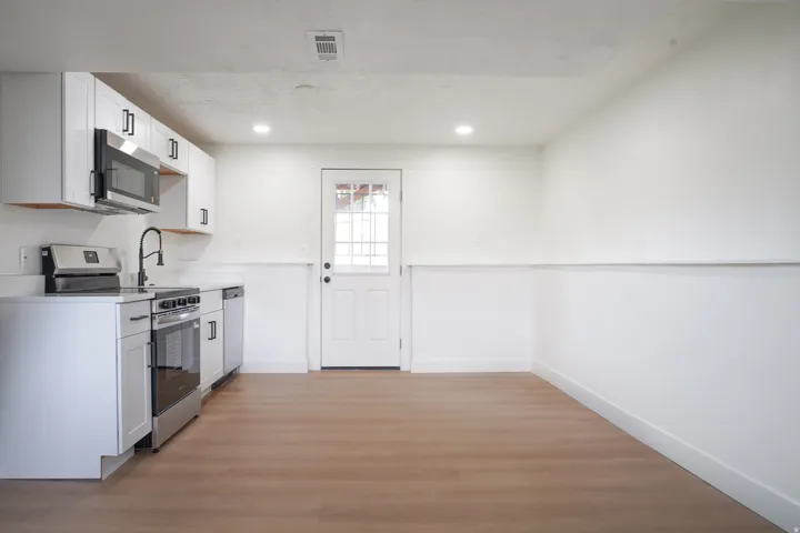 White shaker cabinetry with matte black hardware, stainless steel appliances, wood-finish flooring, recessed lighting, and a paneled door with glass inserts