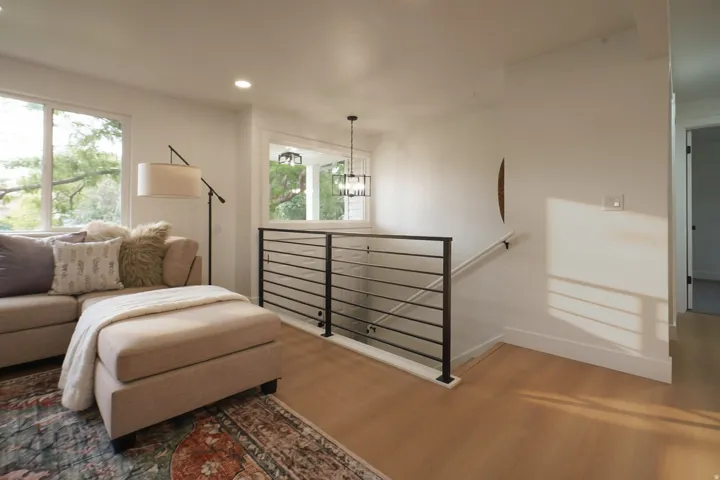 Recessed lighting, large windows, light wood-finish flooring, and black metal stair railing