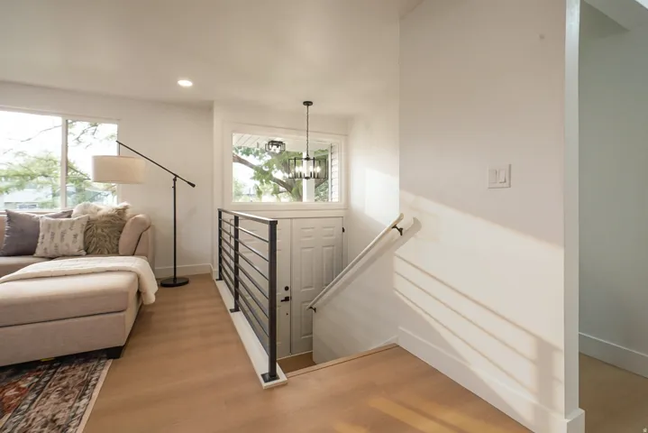 Light wood-finish flooring, white walls, large windows, and contemporary black metal railings