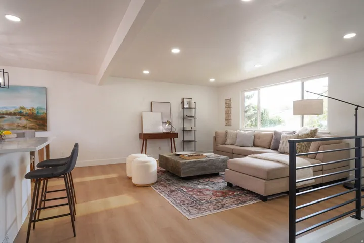 Recessed ceiling lighting, light wood-finish flooring, white walls, large window, and a built-in kitchen island with stone-finish countertop