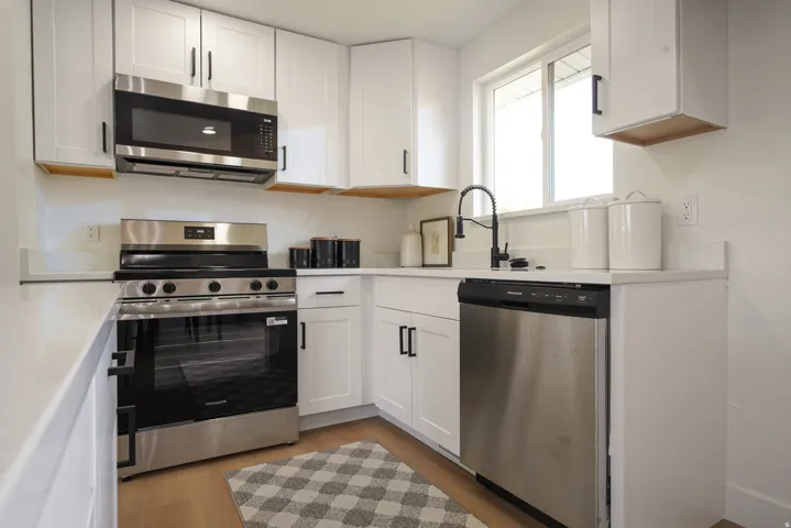 White cabinetry with matte black hardware, stainless steel appliances, light-toned countertops, and a black gooseneck faucet