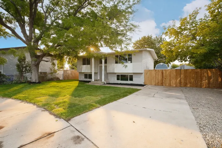 Split-level residence featuring white siding, a concrete driveway, and a wood privacy fence